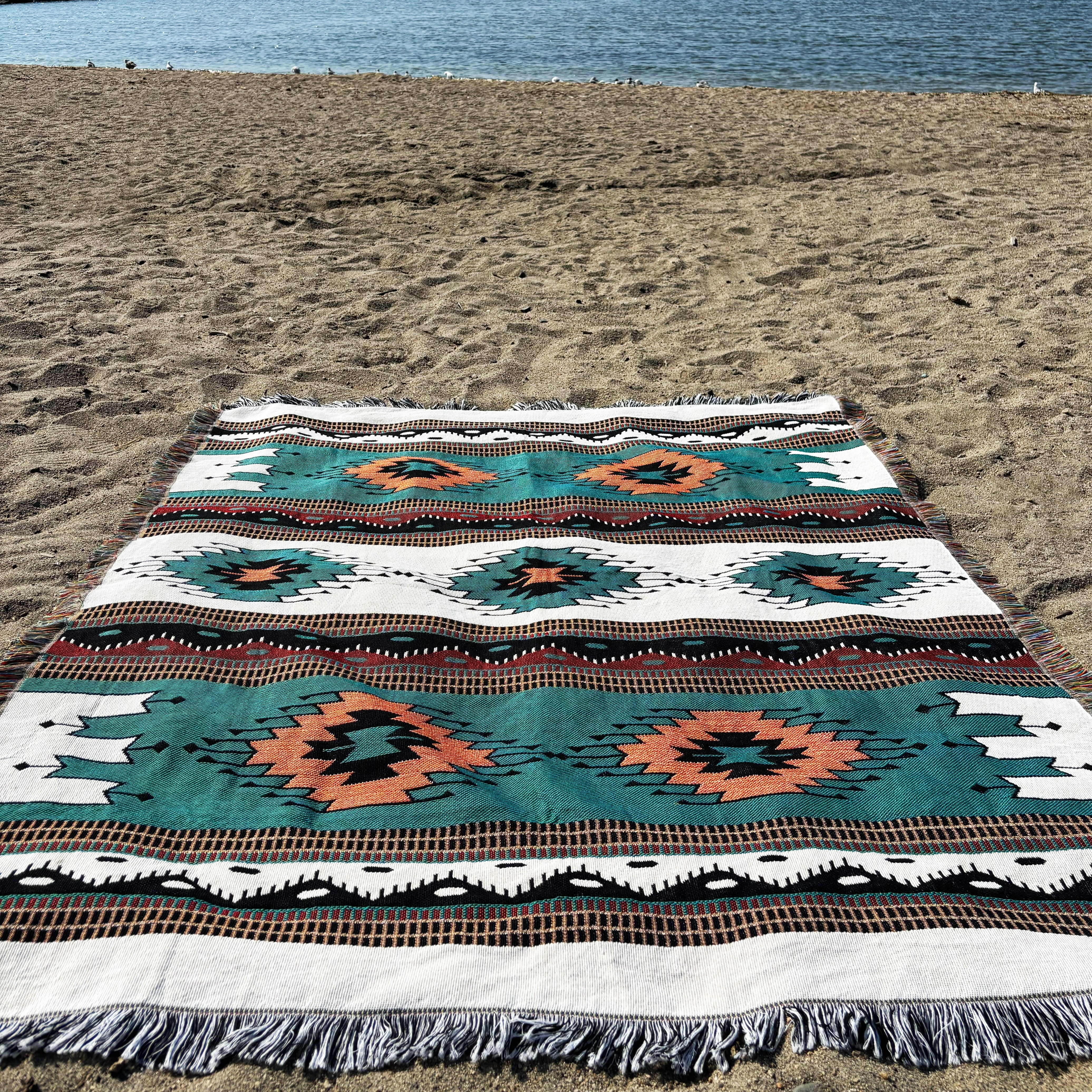 Decorative blanket with geometric pattern on a sandy beach by the water