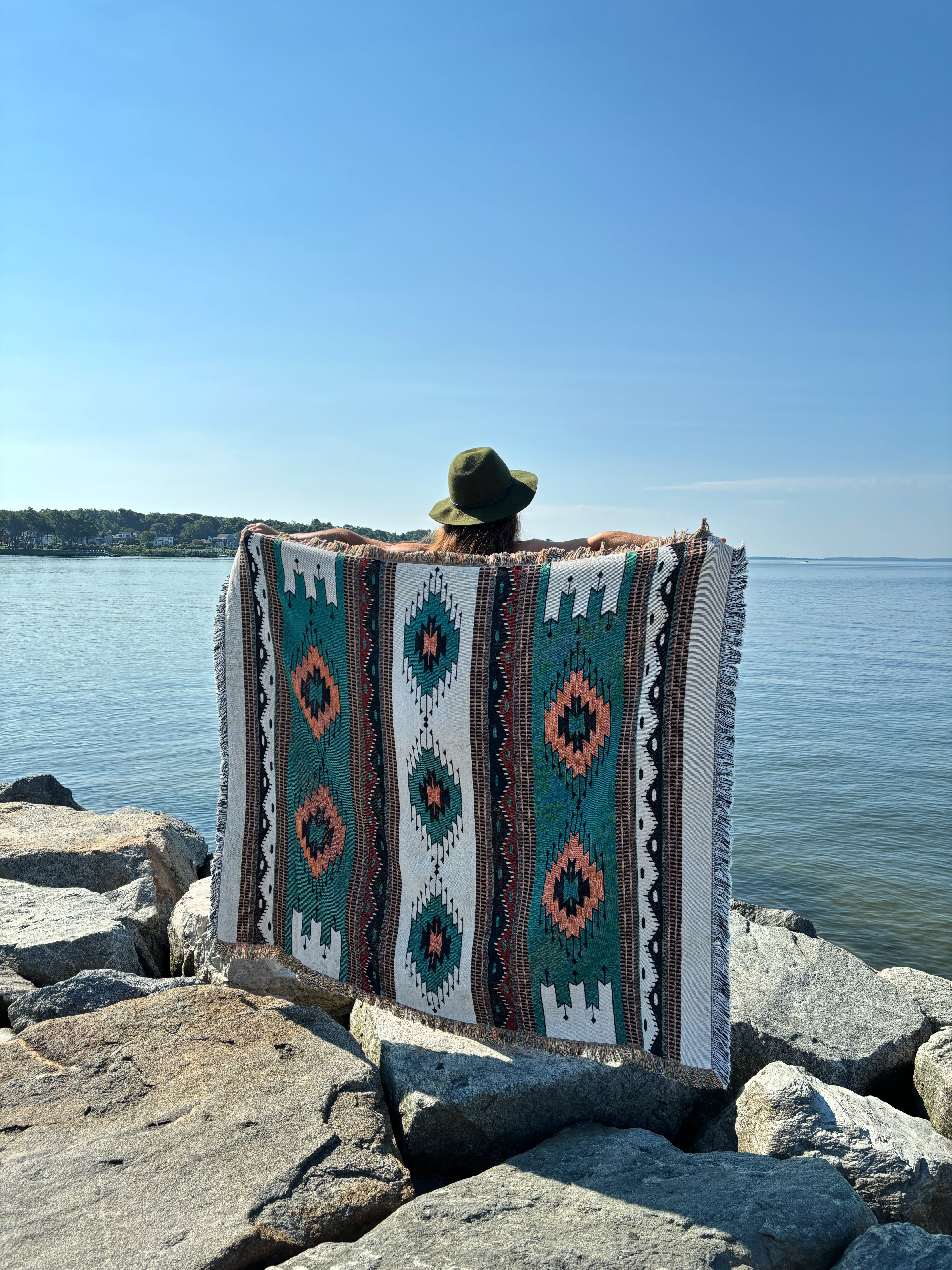 Person sitting on a patterned rug by the water