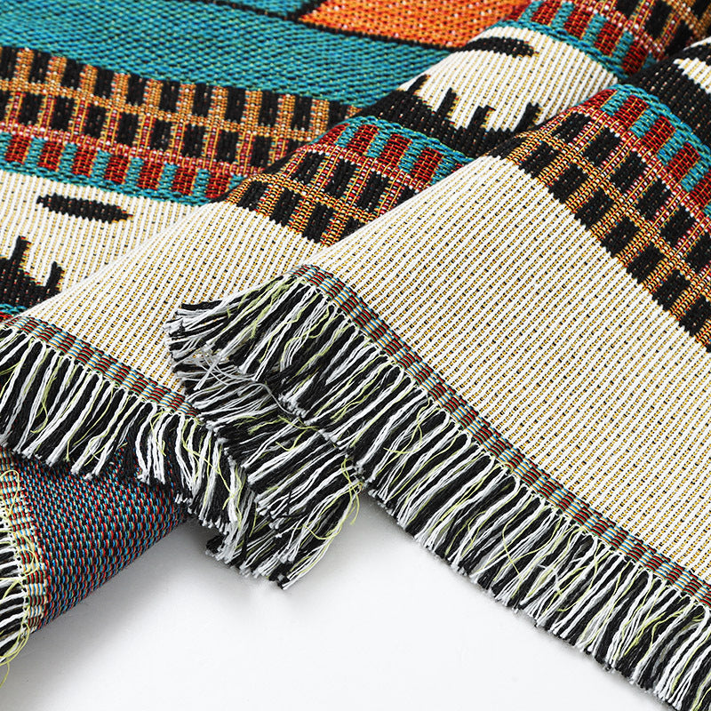 Close-up of a woven textile with geometric patterns and fringes on a white background