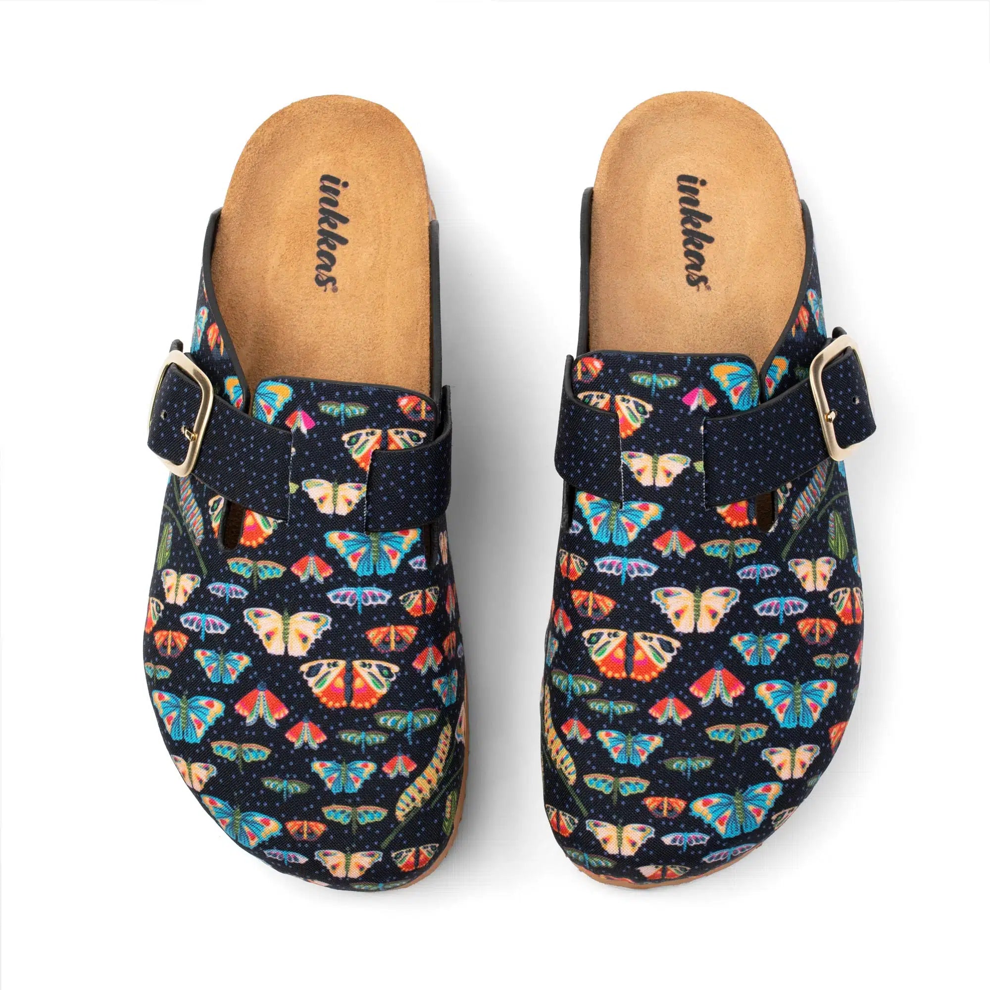 A pair of clog-style mule shoes with a dark navy blue fabric upper covered in a colorful butterfly and moth pattern, featuring a single strap with a gold-tone buckle and a tan insole. The brand name 'Inkkas' is printed on the insole.