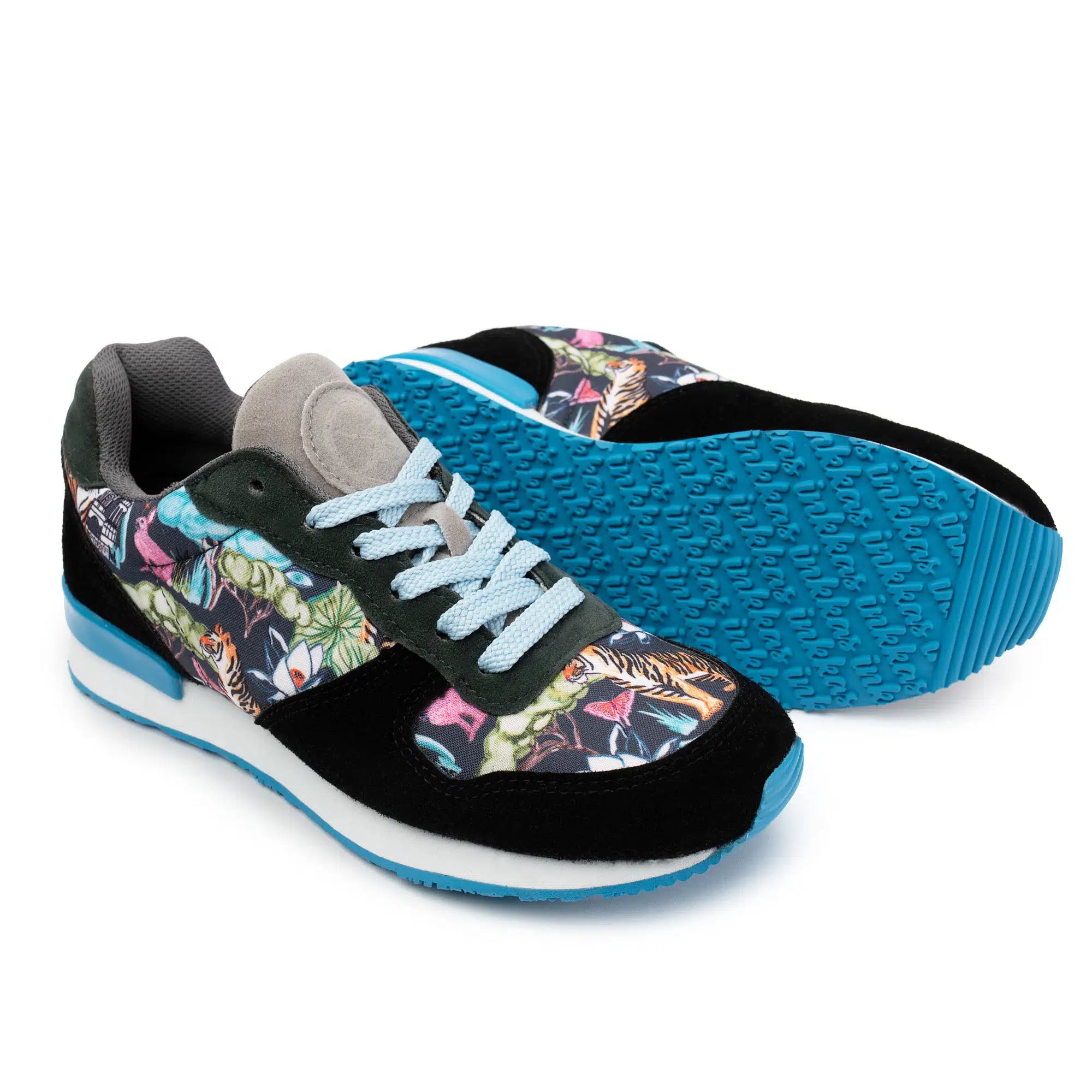 A pair of cushy Joggers shown on a white background, with one shoe standing upright and the other lying on its side to display the sole. The uppers feature a black suede base with a colorful tropical floral and tiger print panel, light blue laces, and a bright blue outsole.