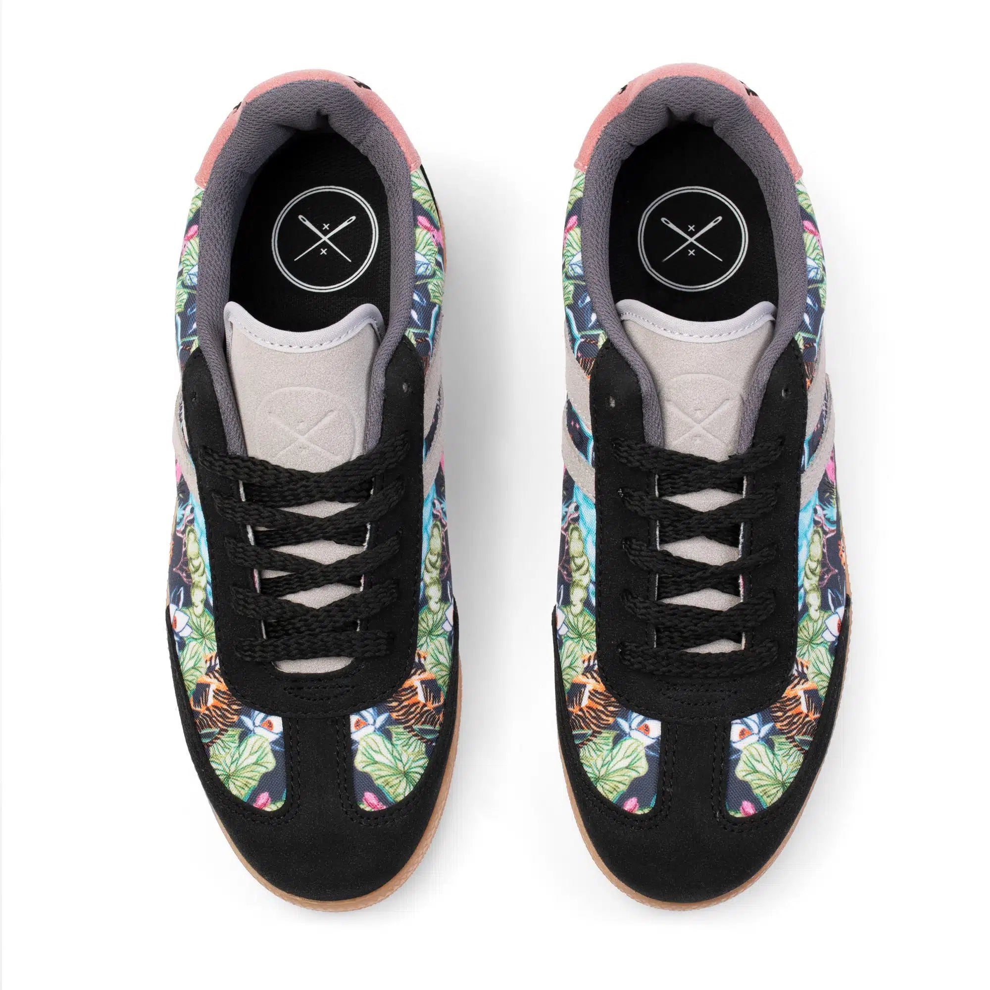 A pair of low-top sneakers shown from a top-down view on a white background. The shoes feature a black suede-like upper with tropical floral and tiger-print panels in green, orange, blue, and pink, black laces, and a light gray tongue.