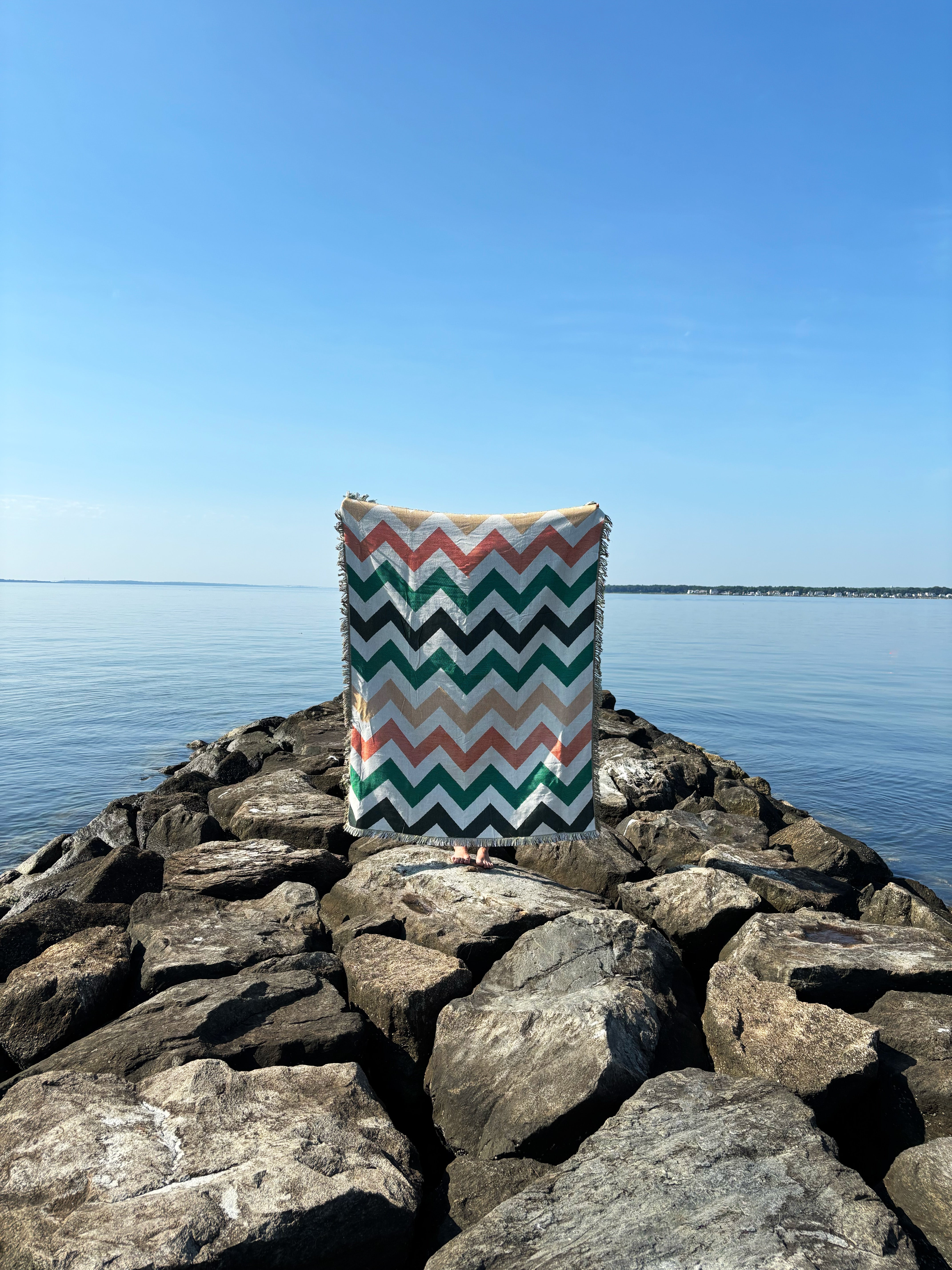 Chevron-patterned bag on rocks by a body of water with clear blue sky