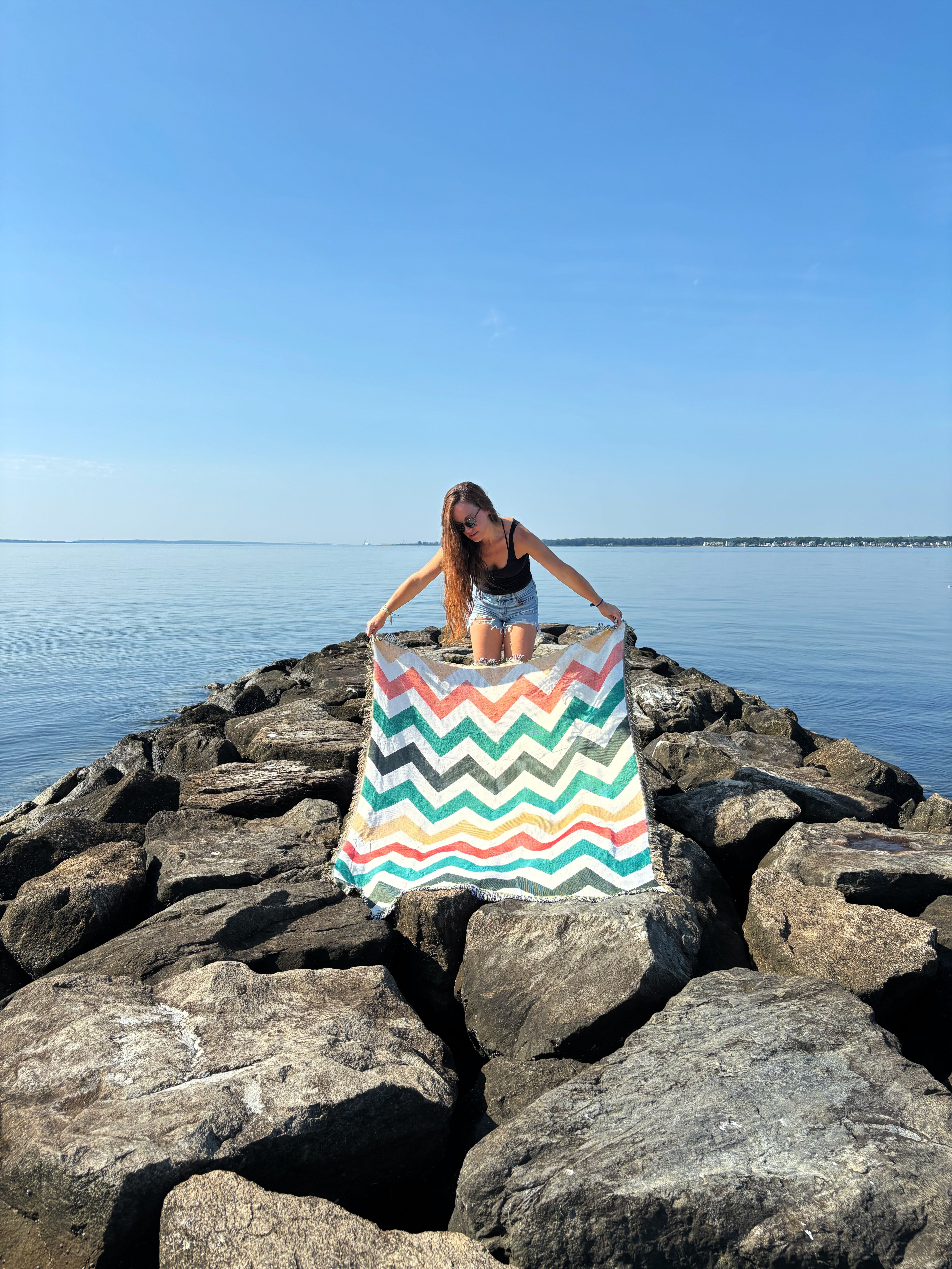 Person holding a colorful striped towel on a rocky jetty by the water
