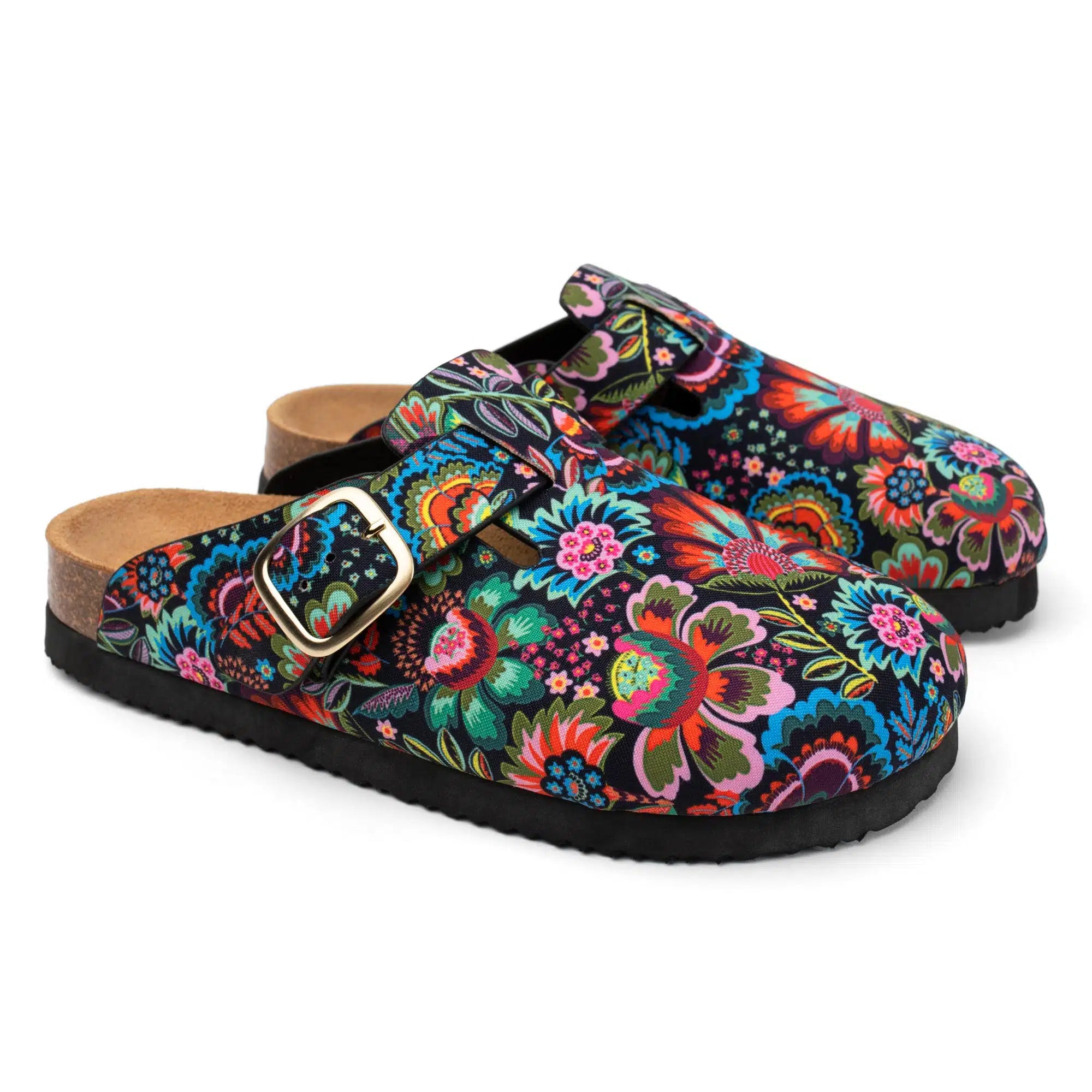 A pair of clog-style mules with a vibrant, multicolored floral and paisley print on a black background, featuring adjustable double straps with gold-tone buckles and a tan cork-like footbed.