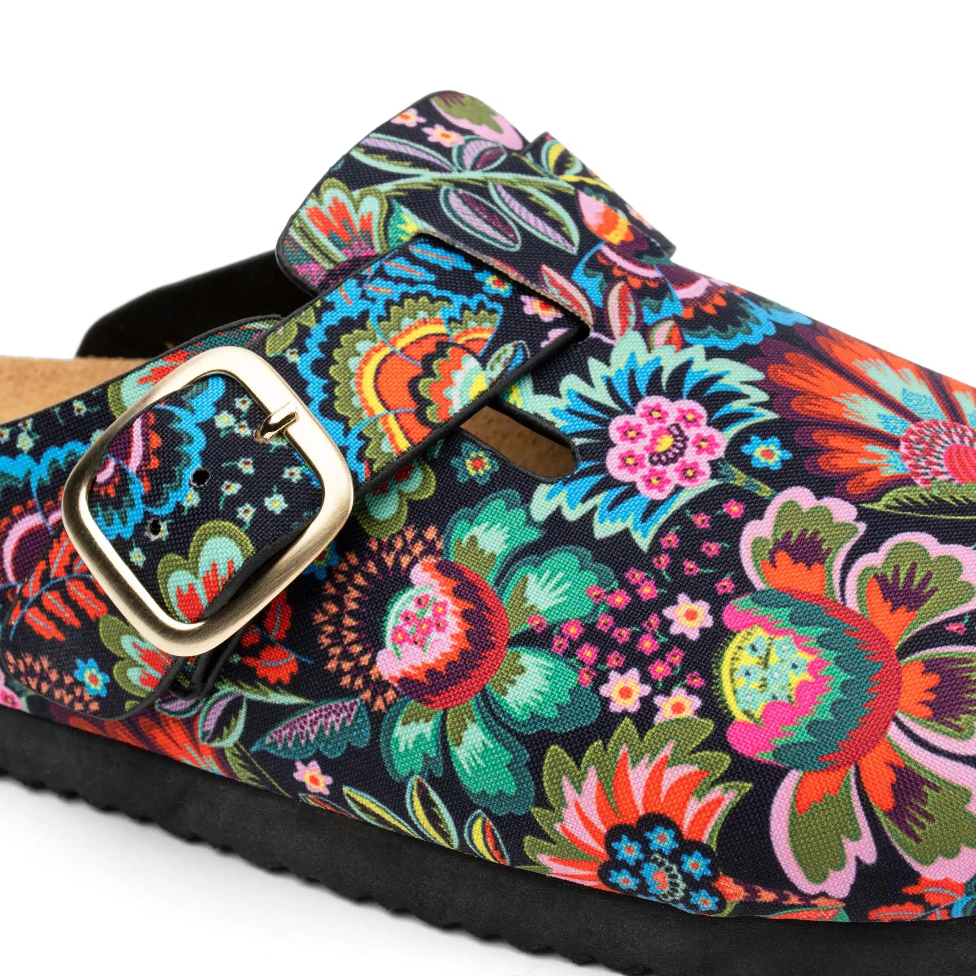 A close-up of a clog-style shoe with a black base covered in a vivid multicolor floral print, featuring a wide strap with a gold-tone buckle.