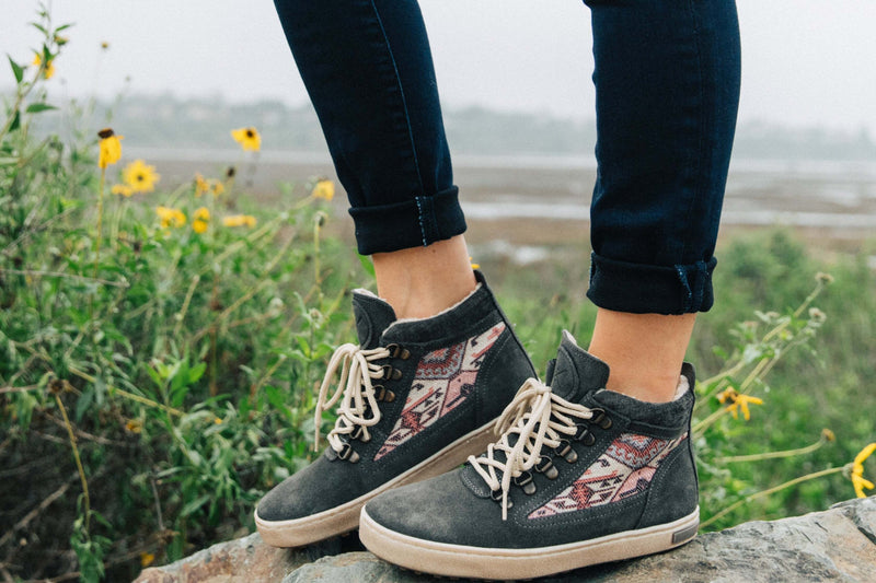The Inkkas Konya Camping Boot, with its woven kilim panel, worn on a rock among wildflowers