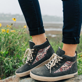 The Inkkas Konya Camping Boot, with its woven kilim panel, worn on a rock among wildflowers