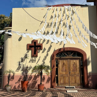 A yellow church in Mexico strung with papel picado banners under a blue sky