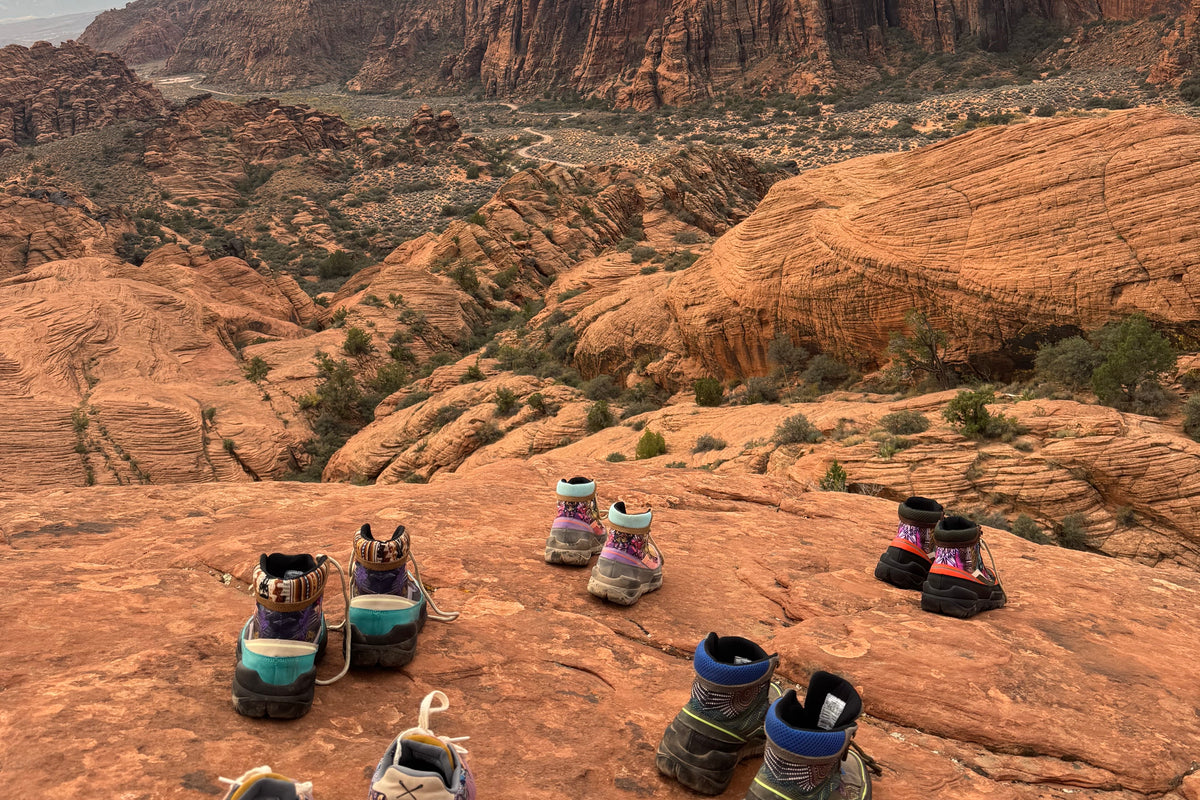 Six pairs of Inkkas trekk boots lined up on red rock at a canyon overlook in Snow Canyon State Park