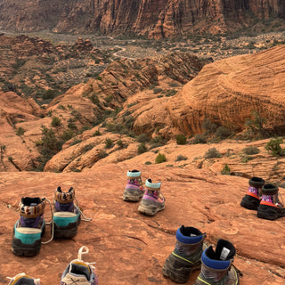 Six pairs of Inkkas trekk boots lined up on red rock at a canyon overlook in Snow Canyon State Park