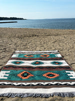 Decorative blanket with geometric pattern on a sandy beach by the water