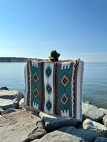 Person sitting on a patterned rug by the water