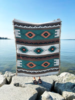 Patterned blanket draped over a person on rocks by a body of water