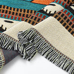 Close-up of a woven textile with geometric patterns and fringes on a white background