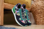 A pair of Inkkas joggers sneakers with a dark navy suede base, teal green overlays, and a colorful floral pattern on the side panels, resting on a wooden surface in a home setting.
