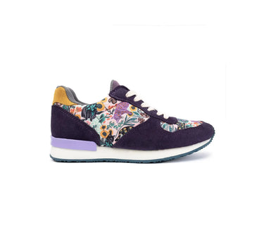 A single low-top sneaker shown in profile against a white background. The shoe features dark purple suede panels, a multicolor floral print overlay on the quarter and toe sections, a yellow heel tab, a light purple midsole accent, and a white midsole.