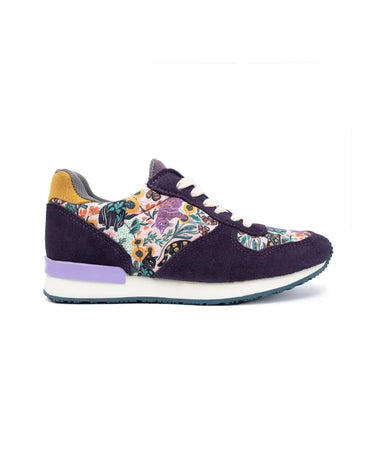 A single low-top sneaker shown in profile against a white background. The shoe features dark purple suede panels, a multicolor floral print overlay on the quarter and toe sections, a yellow heel tab, a light purple midsole accent, and a white midsole.