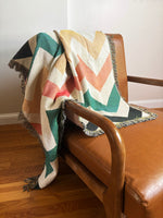 Colorful chevron-patterned blanket draped over a brown leather chair.