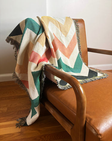 Colorful chevron-patterned blanket draped over a brown leather chair.
