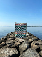 Chevron-patterned bag on rocks by a body of water with clear blue sky