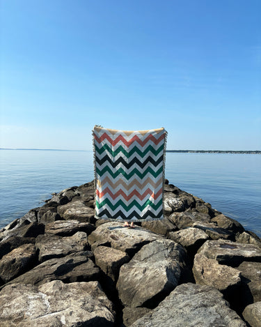 Chevron-patterned bag on rocks by a body of water with clear blue sky