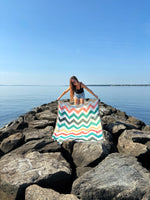 Person holding a colorful striped towel on a rocky jetty by the water