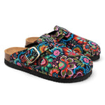 A pair of clog-style mules with a vibrant, multicolored floral and paisley print on a black background, featuring adjustable double straps with gold-tone buckles and a tan cork-like footbed.