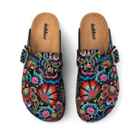 A pair of clog-style mule shoes with a vibrant, multicolored floral print on a black background, featuring a brown insole and a small gold buckle on the side, shown from a top-down view on a white background.